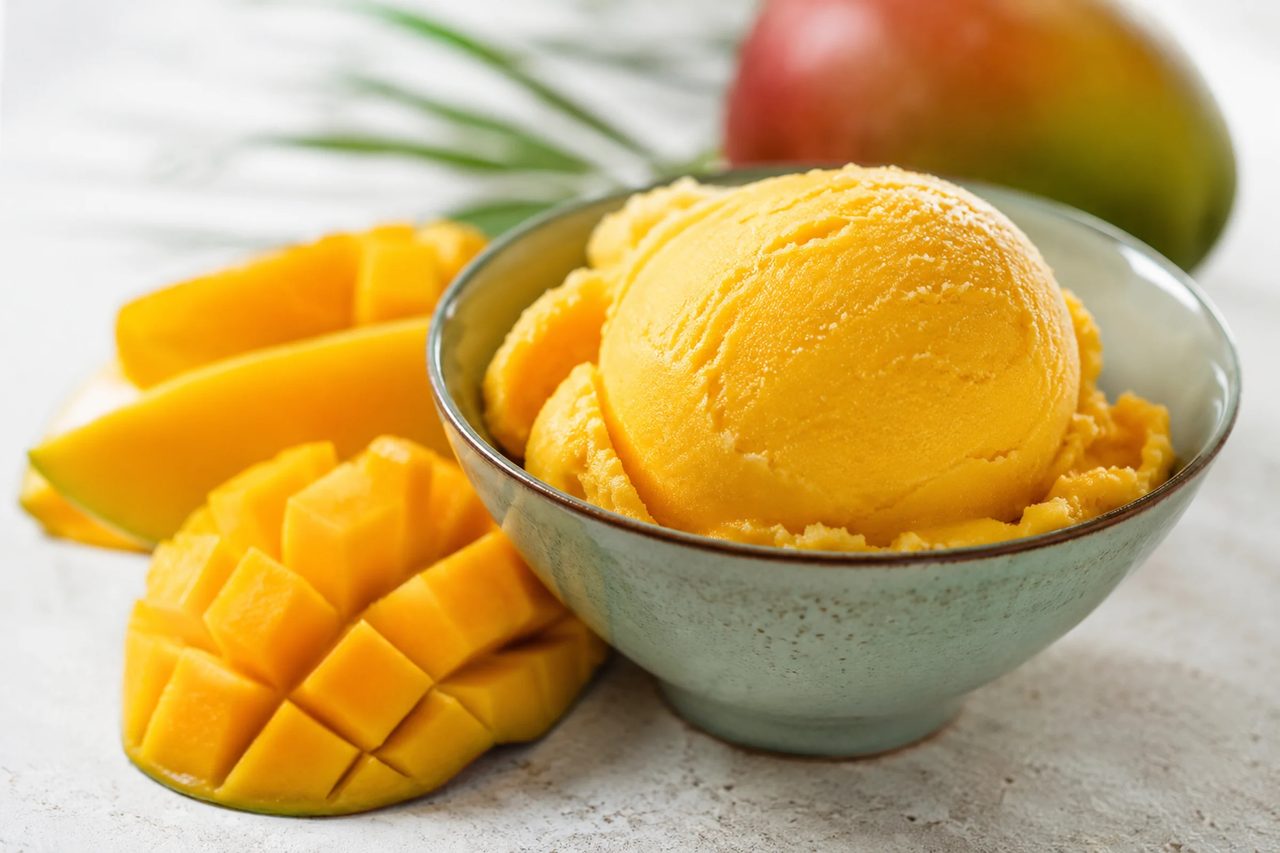 A pint of vibrant golden-orange mango sorbet with soft ripples, scooped into a chilled bowl and finished with a wedge of fresh lime.